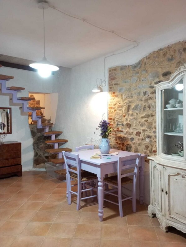 Un espace repas agrémenté d’un mur en pierre, d’un escalier et d’un buffet blanc aux portes vitrées.
