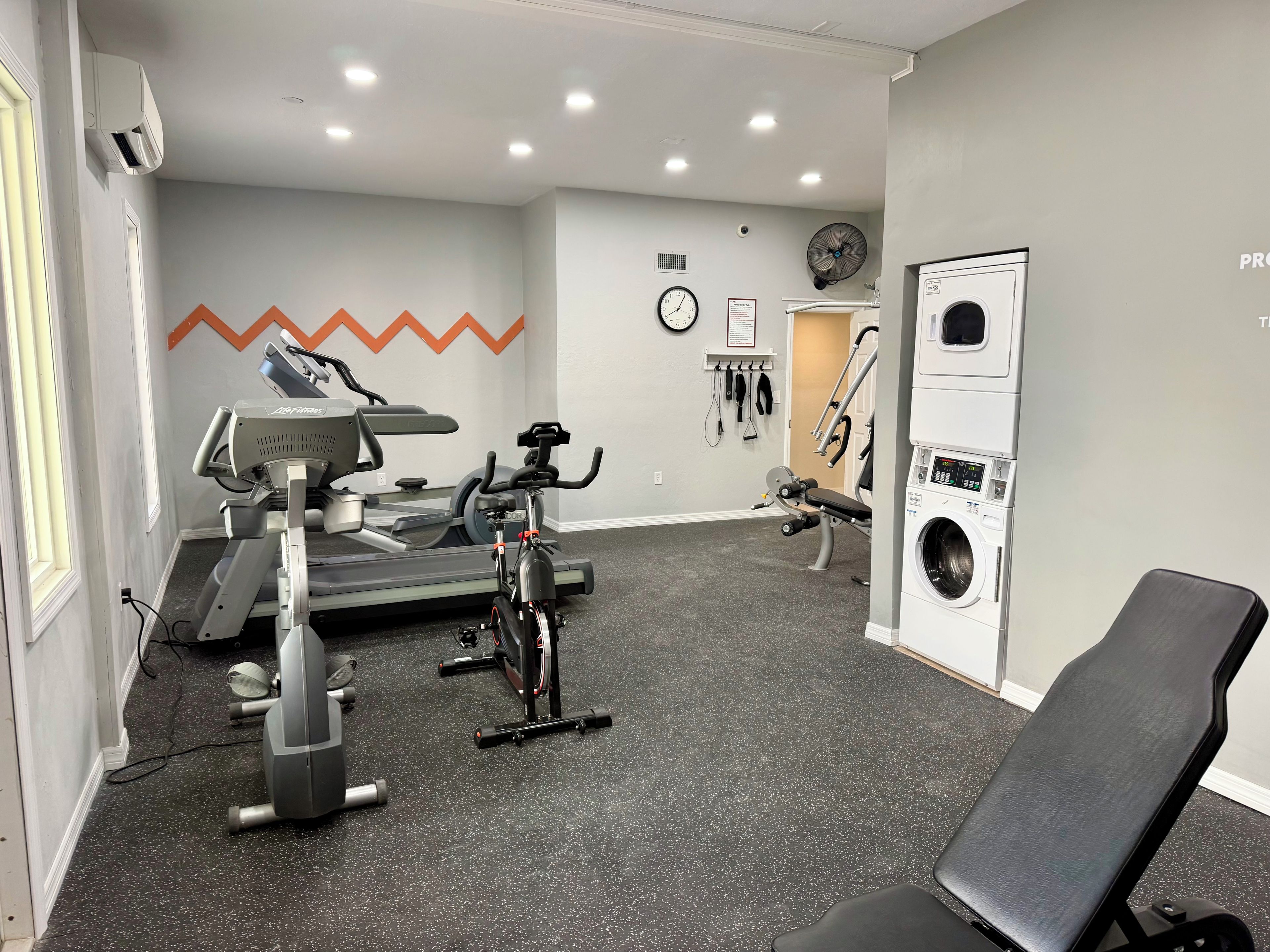 A gym with exercise equipment, a clock, and a washing machine.