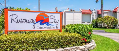 A sign for Runaway Bay Condominium with a landscaped garden and buildings in the background.
