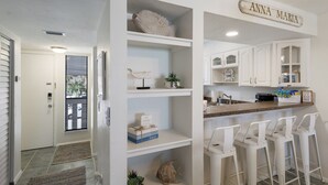 A modern kitchen with white cabinetry, a granite countertop, and a bar area with white bar stools.