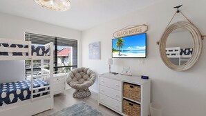 A bedroom with bunk beds, a round chair, a dresser, a mirror, and a beach-themed wall art.