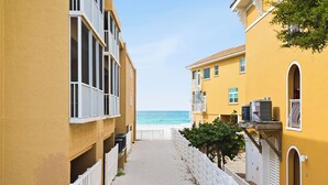 A narrow pathway between yellow buildings leading to a beach.