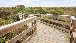 Une promenade en bois mène à un bâtiment doté d’un toit rouge, entouré d’une végétation luxuriante et surplombé d’un ciel dégagé.