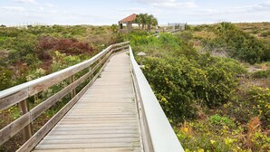 Une promenade en bois mène à une petite construction surmontée d’un toit rouge, qui est elle-même entourée d’une végétation luxuriante.