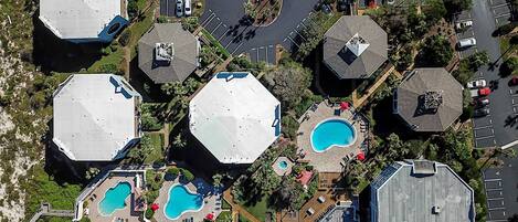 Vue aérienne d’un complexe hôtelier comprenant plusieurs bâtiments hexagonaux, des piscines et un parking.