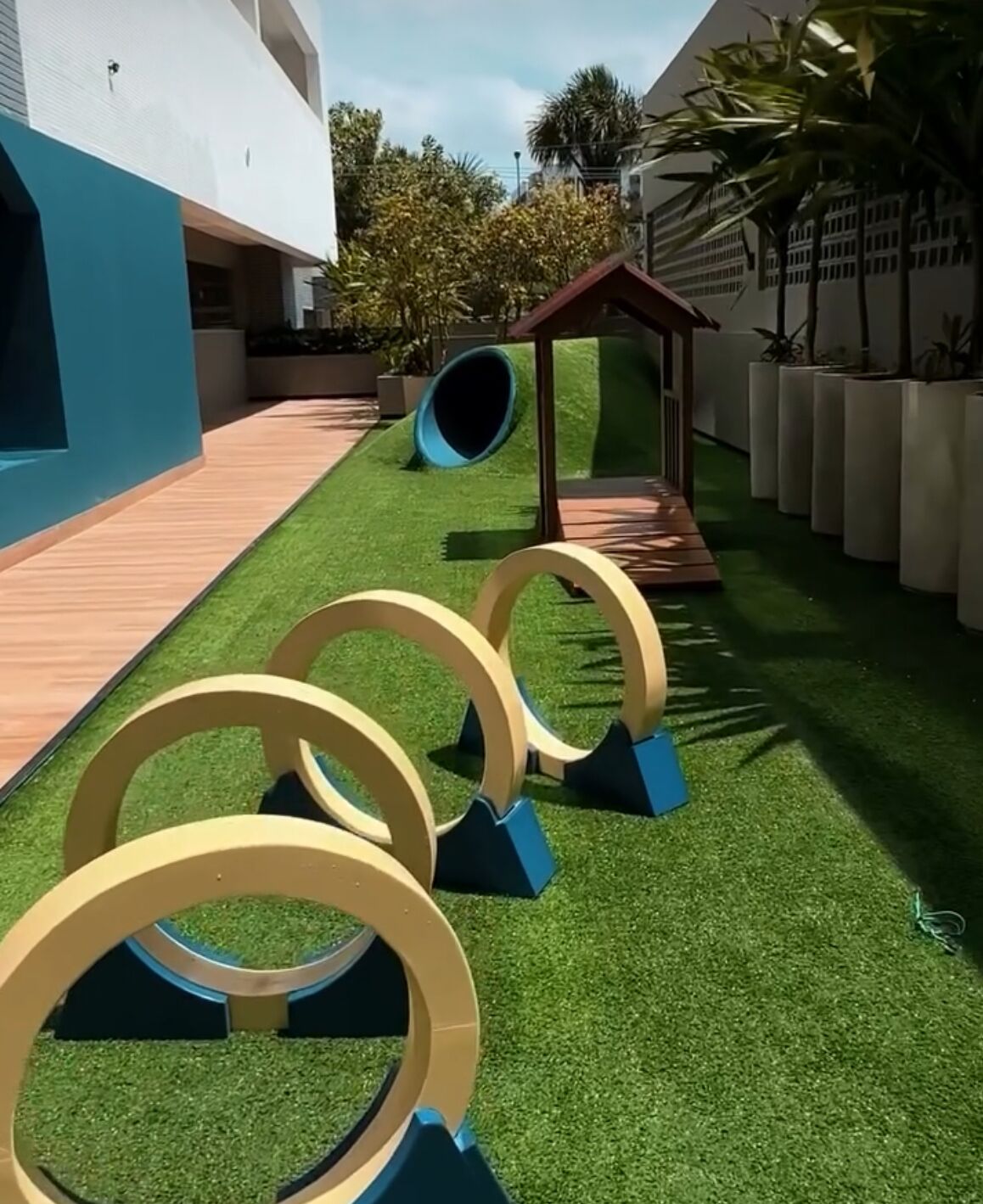 A courtyard with artificial grass, a play structure, and a series of circular obstacles.