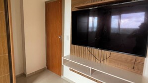 A room with a large flat-screen TV mounted on a wooden panel wall, a white entertainment unit below, and a wooden door. - Breeze Residence duplex penthouse, Belém do Pará, for cop30 (Val-de-Cans Belém)