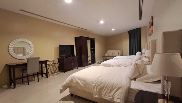 Una camera d'albergo con un letto grande, una scrivania con una sedia, una televisione, un armadio e una lampada.