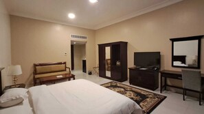 A hotel room with a bed, a desk, a television, a wardrobe, and a mirror. - Mafaza Al-Qassim Hotel (Riyad Al Khabra)