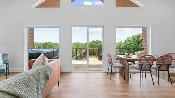 Een ruime kamer met een hoge plafond, een balkon met een houten terras, en een eethoek met stoelen en een tafel.