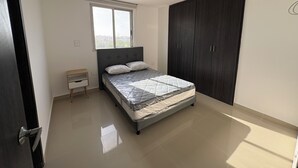 A bedroom with a bed, a window, a small bedside table, and a wardrobe.