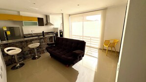 A modern kitchen with a built-in stove, a dining area with a dark brown sofa, and a yellow chair.