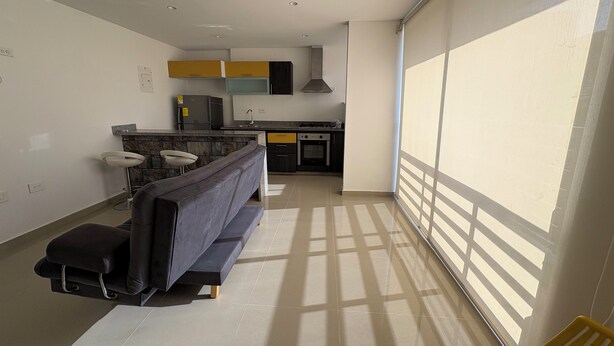 A modern kitchen with a built-in oven, a sink, and a stove. There is a seating area with a sofa and a chair.