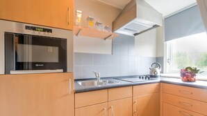 A modern kitchen with wooden cabinets, a built-in oven, a stainless steel sink, and a window with a view of greenery. - Holiday Home in Elim for Family (Elim)