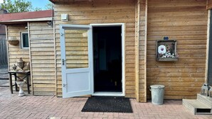 A wooden cabin with a large open door, a welcome sign, and a small table with pots outside. - Holiday Home in Elim for Family (Elim)