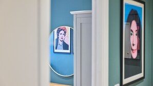 A hallway with framed artwork on the walls, a white door, and a wooden floor.