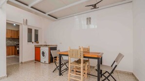 A compact kitchen with a washing machine, a dining table with chairs, and a ceiling fan. - A beautiful apartment for rent with everything you need. (Essaouira)