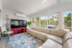 A living room with a large flat-screen TV, a beige sofa, a red entertainment unit, and a patterned rug.