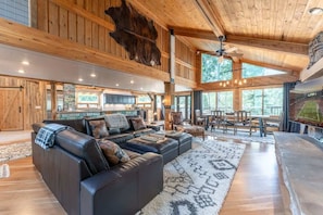 A spacious living room with a large leather sofa, wooden ceiling beams, and a stone fireplace.