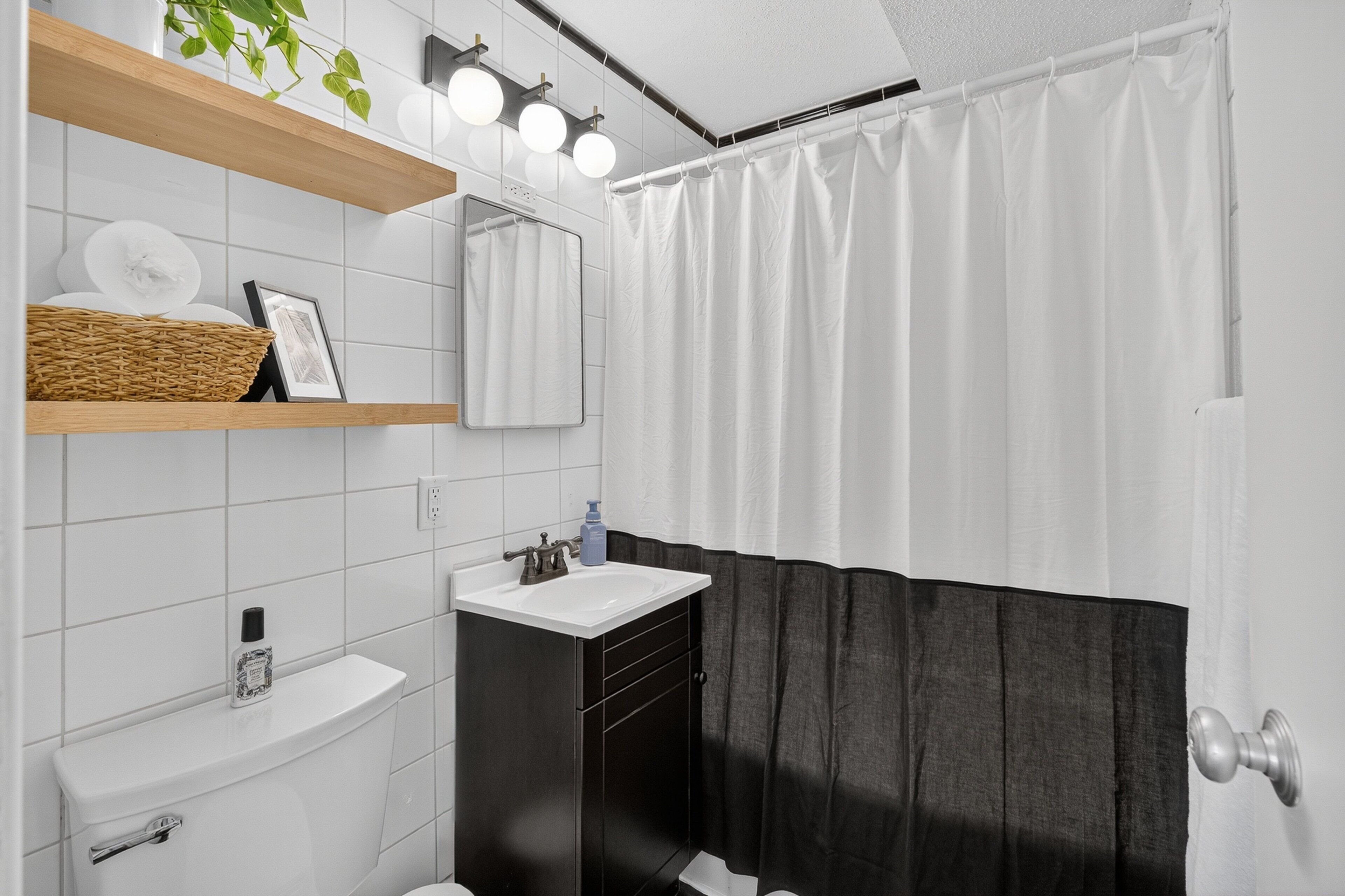 Un bagno con un lavandino bianco, un armadietto nero e una tenda da doccia.