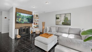 Ein modernes Wohnzimmer mit einem grauen Ecksofa, einem Flachbildfernseher an einer Holzvertäfelung, einem Kamin und einem großen abstrakten Gemälde an der Wand.