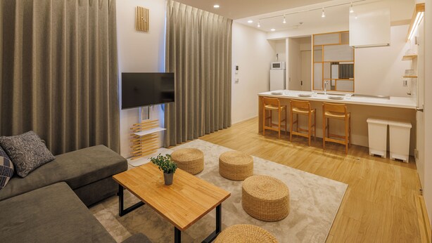 Una sala de estar moderna con un sofá, una mesa de centro de madera y un televisor. Hay una zona de cocina con un microondas y un lavamanos.