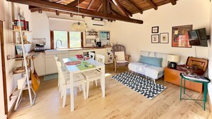 Een gezellige, goed verlichte kamer met een houten plafond, een eethoek met tafel en stoelen, een bank en een klein bijzettafeltje.
