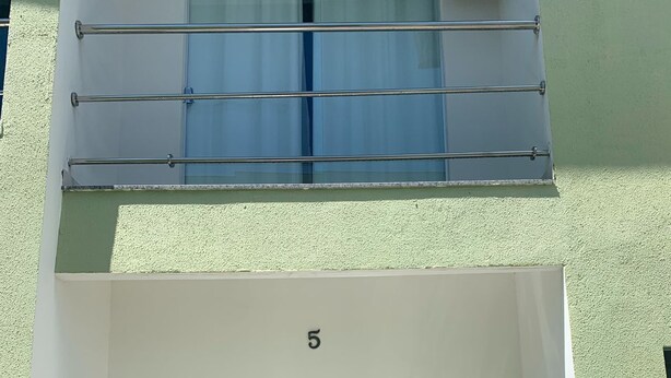 En balkon med gelændinger, en glasdør med gardiner og en lille stol.