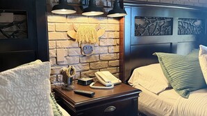 A hotel room with a brick wall, two beds with white bedding, a wooden nightstand with a phone and lamp, and a mounted picture of a cow. - Ideal Condo in River Ranch • Across from the water park and near the rodeo (River Ranch)