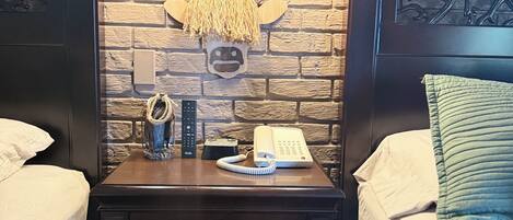A hotel room with a brick wall, a headboard with a hornet design, two bedside tables with lamps, a telephone, and a decorative hornet head.