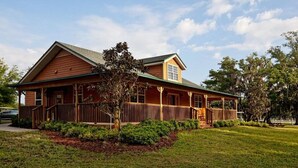 A two-story wooden house with a porch, surrounded by a well-maintained lawn and trees. - Ideal Condo in River Ranch • Across from the water park and near the rodeo (River Ranch)