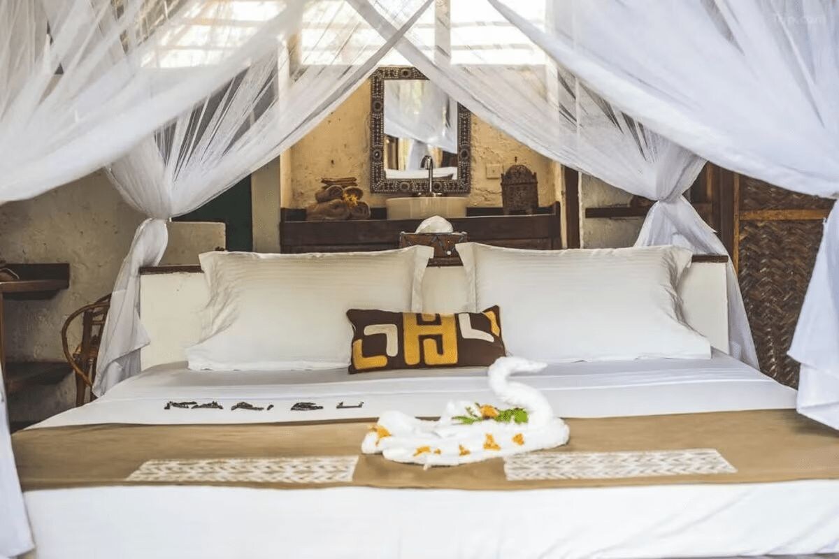 A bed with white linens, a swan-shaped towel, and a decorative pillow with a golden pattern.