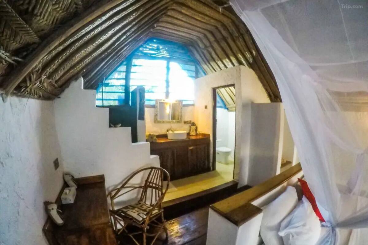 Ein rustikales Zimmer mit Holzbalkendecke, einem kleinen Holztisch, einem Korbstuhl und einem Bett mit weißen Leinentüchern.