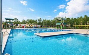 A swimming pool with multiple lanes, surrounded by trees and a clear sky.