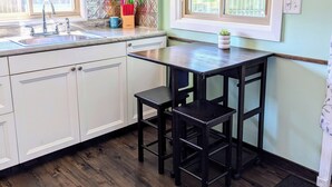 A kitchen with white cabinets, a sink, a window, and a clock on the wall. - Cozy Haven - Little Lakefront Home (Little Lake)