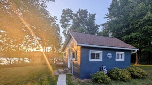 A small house with a 'Welcome to Lake House' sign, a concrete pathway leading to the entrance, and a grassy yard. - Cozy Haven - Little Lakefront Home (Little Lake)