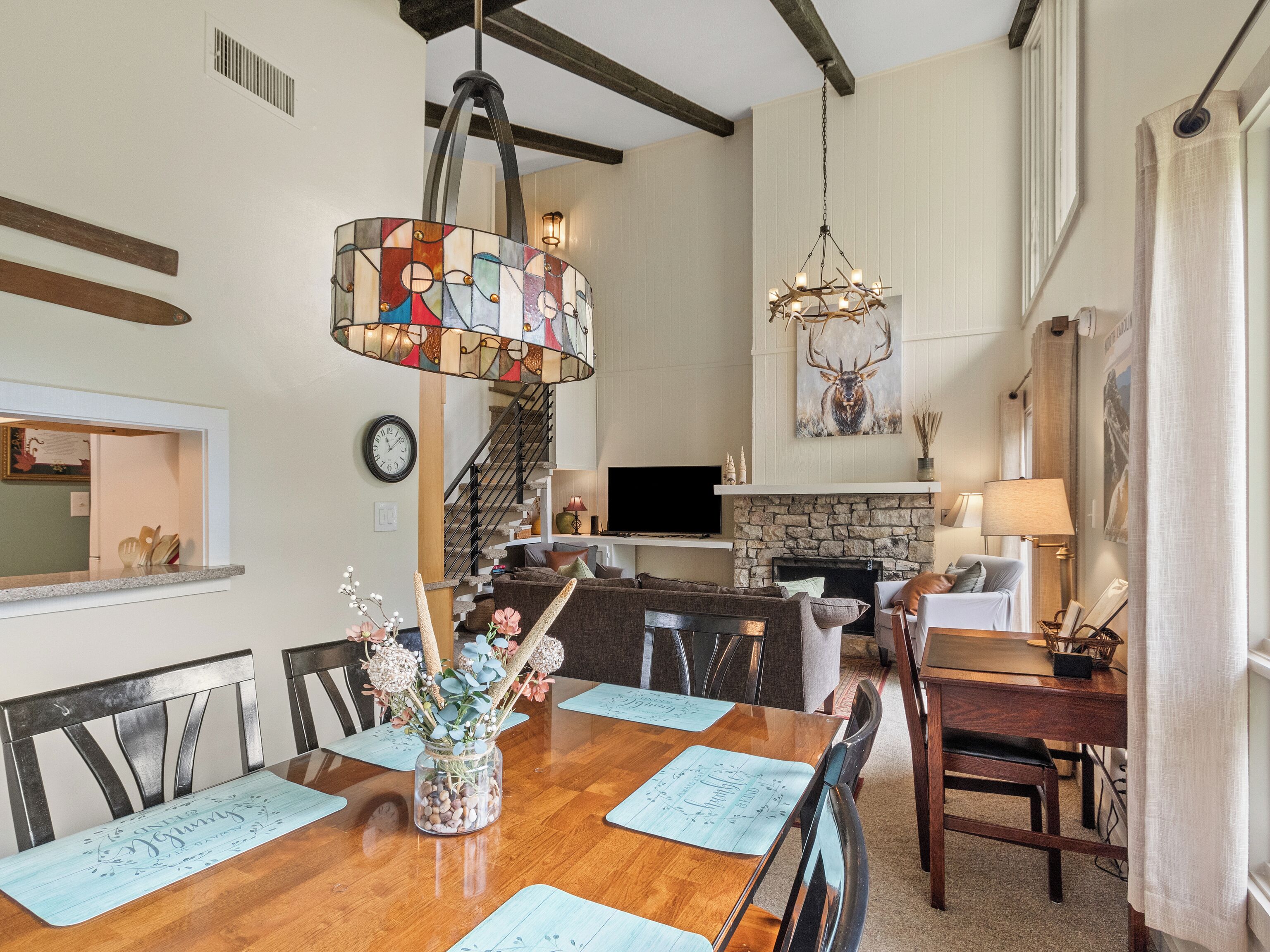 A spacious living room with a fireplace, a dining area with a wooden table, and a kitchen area with a stone fireplace.