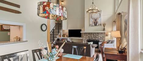 A spacious living room with a fireplace, a dining area with a wooden table, and a kitchen area with a stone fireplace.