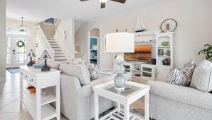 A living room with a staircase, white furniture, and a TV.
