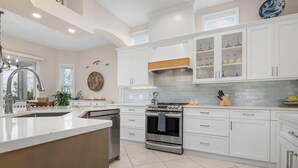 A modern kitchen with white cabinetry, a stainless steel stove, and a large island with a sink.