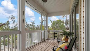 A covered porch with a wooden floor, white railings, a table with chairs, and a potted plant.
