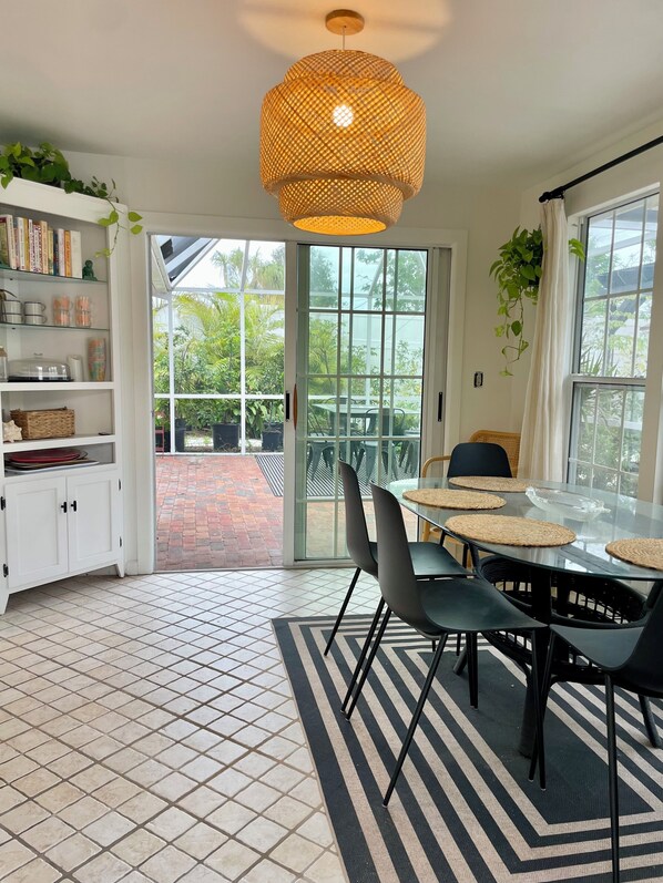 A modern kitchen with a dining area, featuring a large window, a hanging light fixture, and a tiled floor.
