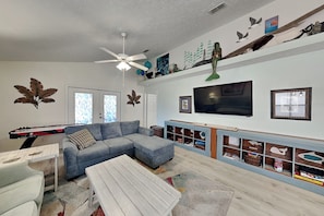 A living room with a sectional sofa, a coffee table, a television, and a ceiling fan.