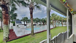 A pool area with a fence, palm trees, and a view of houses in the background. - Captain Bennett's Cove | 1mi to Beach + Community Pool (Panama City Beach)