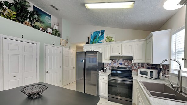 A kitchen with white cabinets, a stainless steel refrigerator, an oven, a microwave, and a black countertop. - Captain Bennett's Cove | 1mi to Beach + Community Pool (Panama City Beach)