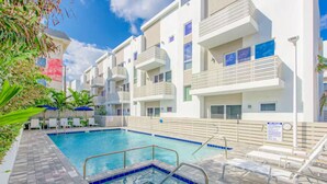 Un espace piscine doté d’une terrasse carrelée, de chaises longues et d’un bâtiment avec des balcons.