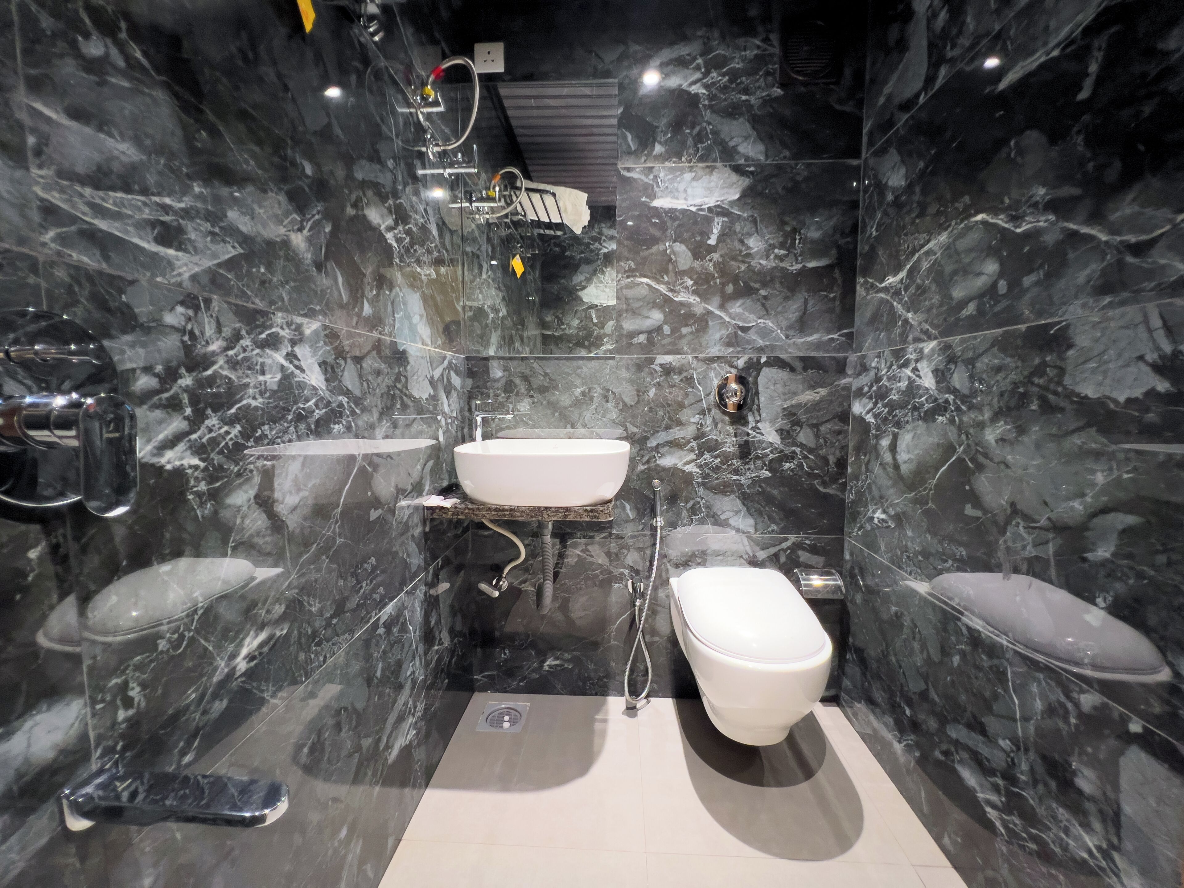 A modern bathroom with a white sink, toilet, and bidet, all set against dark marble walls.