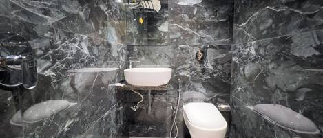 A modern bathroom with a white sink, toilet, and bidet, all set against dark marble walls.