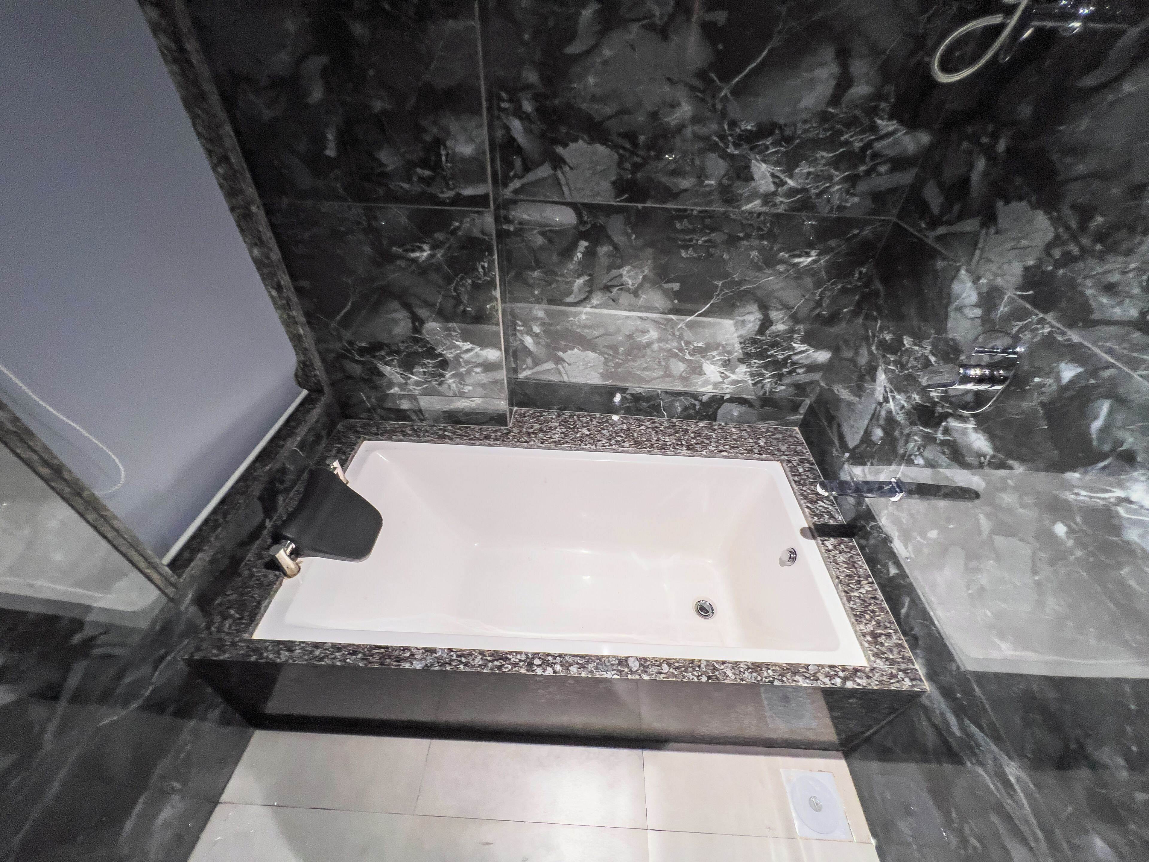 Une salle de bain avec une baignoire blanche, des murs en marbre foncé et un comptoir en granit.