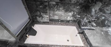 Une salle de bain avec une baignoire blanche, des murs en marbre foncé et un comptoir en granit.